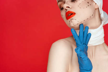 portrait of a woman in blue gloves syringe in hands contour on the face lifting red backgroundの写真素材