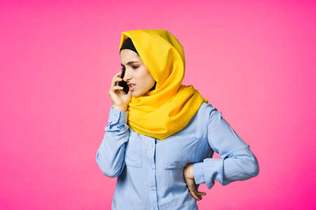 muslim woman in yellow hijab talking on the phone technology pink backgroundの写真素材
