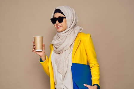 woman in sunglasses in hijab a cup of coffee beige backgroundの写真素材