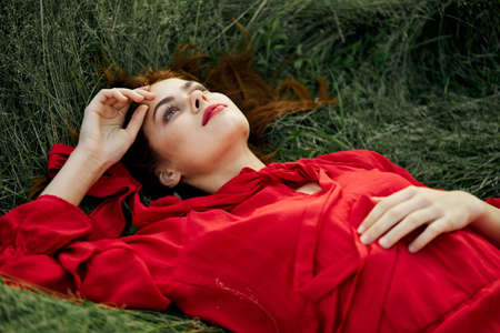 woman in red dress lies on the grass address fashion summerの写真素材