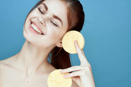 woman with sponges in hands bare shoulders clear skin blue backgroundの写真素材