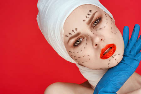 beautiful woman in blue gloves syringe in hands contour on the face lifting red backgroundの写真素材