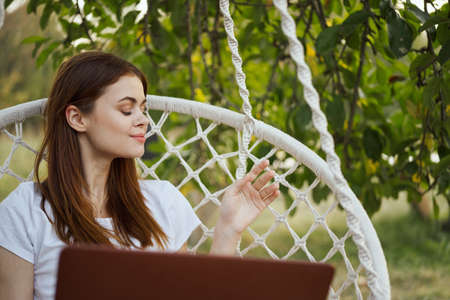smiling woman outdoors in hammock with laptop technologyの写真素材
