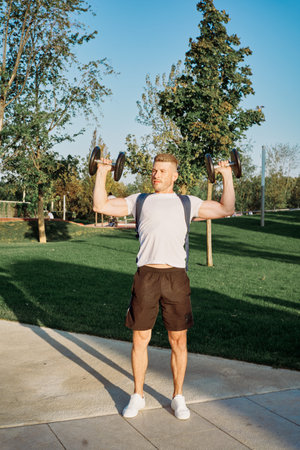 athletic man with dumbbells outdoors at CrossFit park