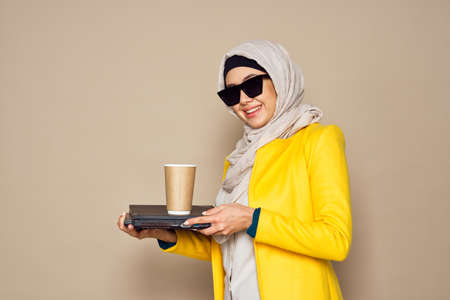 woman in sunglasses in hijab a cup of coffee beige backgroundの写真素材