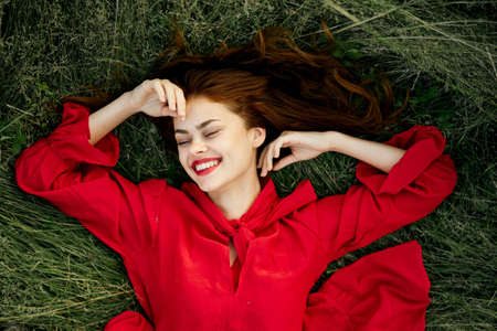 cheerful woman in a red dress lies on the grass top viewの写真素材