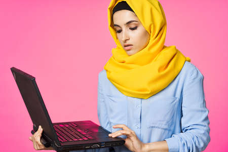 muslim woman in yellow hijab with laptop technology student pink backgroundの写真素材