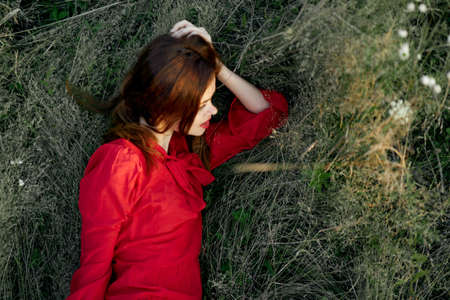 pretty woman in red dress lies on the grass posing top viewの写真素材