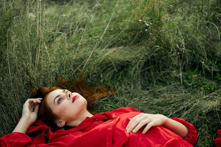 pretty woman in red dress lies on the grass freedom landscapeの写真素材