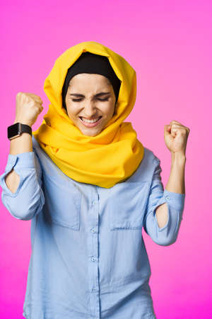 cheerful woman in yellow hijab electronic watch technology user pink backgroundの写真素材