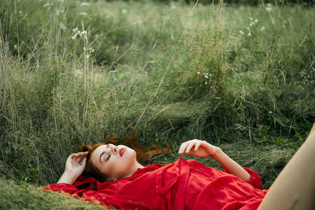 pretty woman in red dress lies on the grass freedom landscapeの写真素材
