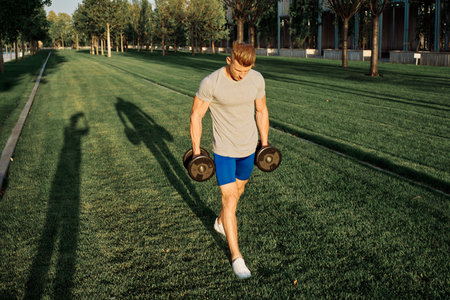 athletic man in the park workout exercise dumbbells