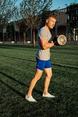 athletic man in the park workout exercise dumbbells
