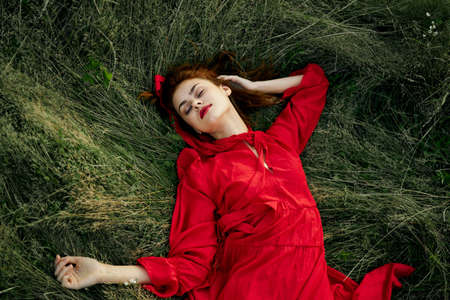 woman in red dress lies on the grass in the field nature landscapeの写真素材