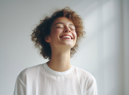 Cheerful African American Woman with Curly Hair, Smiling, and Relaxing against a White Wallの素材