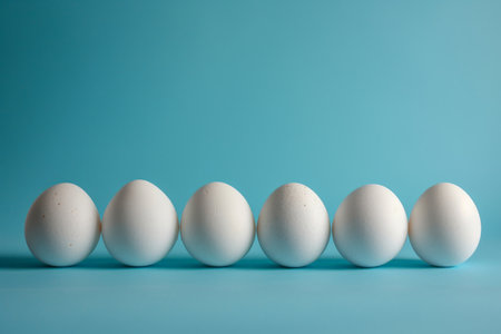 Five white eggs lined up in a row on a blue background with copy space, minimalistic conceptの素材