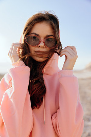 Relaxing day at the beach woman in pink hoodie and sunglasses with hands on head by the waterの写真素材