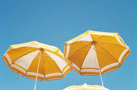 Yellow and white beach umbrellas against a bright blue sky, creating a vibrant summer sceneの素材