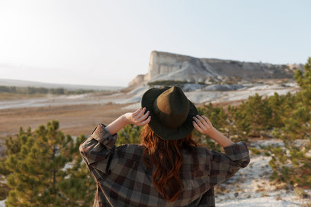 female hiker in plaid shirt and hat gazing at majestic mountain landscape