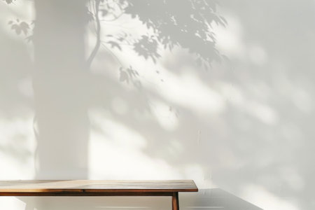 Wooden bench casting shadows on a white wall, featuring the play of light and leavesの素材