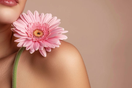 A close up of a woman s shoulder adorned with a pink gerbera daisy against a soft beige backgroundの素材