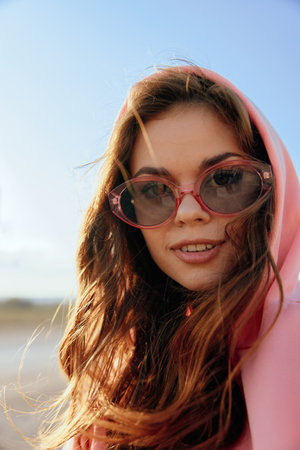 Summer vibes woman in pink hoodie and sunglasses enjoying the beach on a sunny dayの写真素材