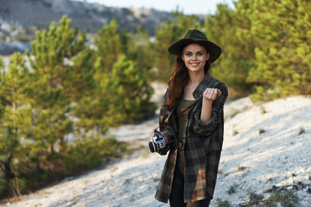 Woman in plaid shirt and hat capturing natures beauty with camera on hilltopの写真素材
