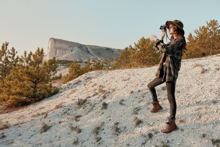 Capturing the majestic mountain woman photographing scenic landscape from hilltop on sunny dayの写真素材