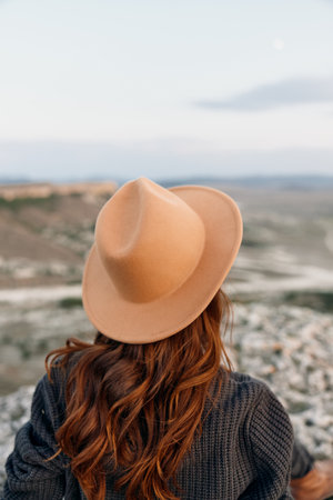 Woman in hat sitting on rock overlooking valley with majestic mountain backdropの写真素材