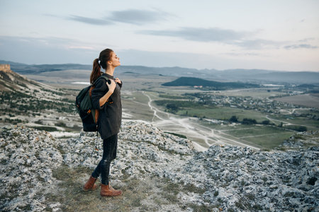 adventurous woman standing triumphantly atop a majestic mountain, gazing out over a breathtaking valleyの写真素材
