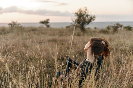 Solitude and contemplation woman sitting in tall grass at sunset with head in hands gazing at horizonの写真素材