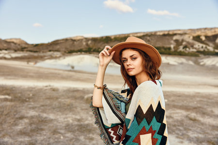 Woman in hat and poncho standing in desert landscape with mountains