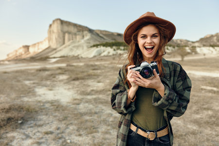 Smiling woman in hat capturing scenic mountain view with camera in handの写真素材