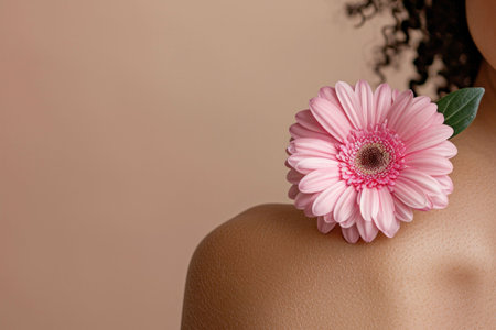A close up of a woman s shoulder adorned with a pink gerbera daisy against a soft, neutral backgroundの素材