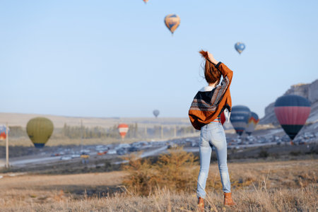 Woman standing in grass with arms up watching colorful hot air balloons in the skyの写真素材