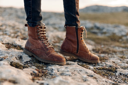 Woman in brown boots on rocky hillside with hands in air celebrating nature and freedomの写真素材