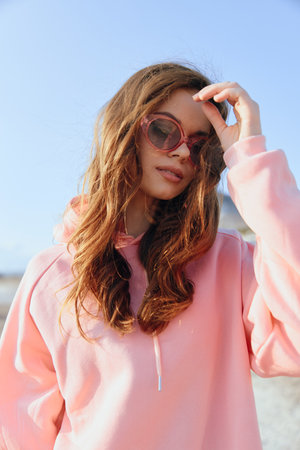 Stylish young woman in pink sweatshirt and sunglasses enjoying a sunny day at the beachの写真素材