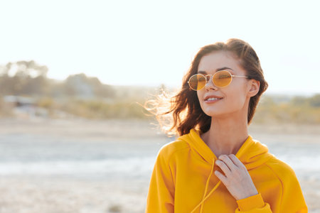 Confident woman in yellow sweater and sunglasses poses with hands on hips in desert landscapeの写真素材