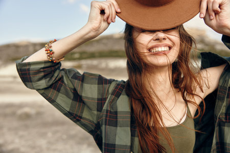 Stylish woman with ponytail holding on to her chic hat against a blurred background