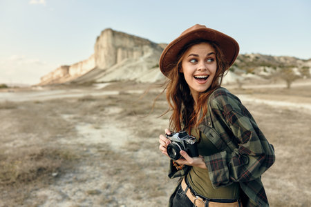 happy woman in hat capturing stunning mountain view with cameraの写真素材