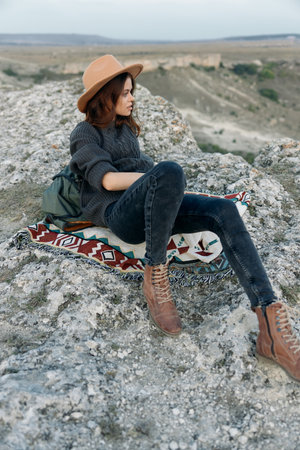 Serene woman in hat relaxing on rock with blanket on a sunny dayの写真素材