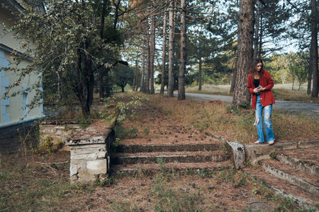serene woman in red jacket standing on forest steps surrounded by tall treesの写真素材