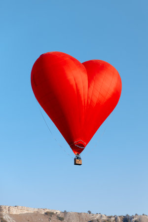 heart shaped balloon soaring over sunny hillside with clear blue sky backgroundの写真素材