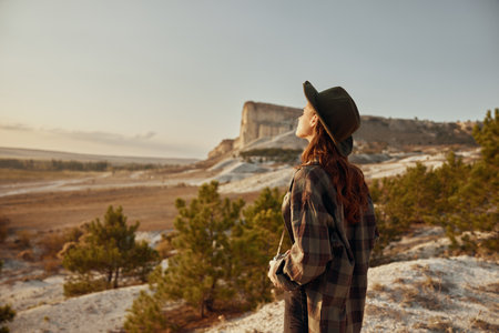 Woman in plaid shirt and hat standing on hill overlooking beautiful valley landscapeの写真素材
