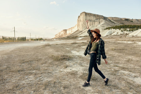 Euphoric woman in hat raises arms in celebration while walking through expansive desert landscapeの写真素材