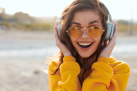 Stylish woman in yellow sweater and sunglasses listens to music with headphones on her headの写真素材