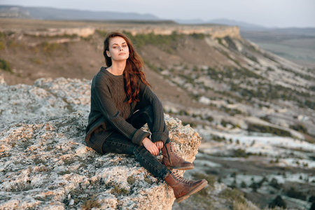 Serene woman sitting on rocky mountaintop with hands on knees, enjoying scenic view