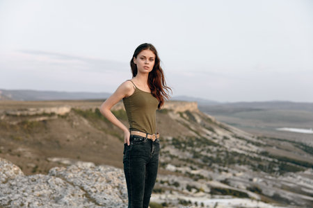 Woman in tank top and jeans stands atop mountain, overlooking picturesque valley belowの写真素材
