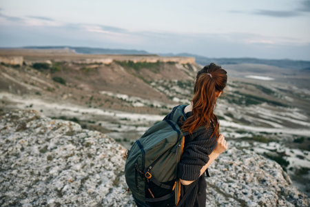 adventurous woman standing atop mountain peak, gazing out at sprawling valley below