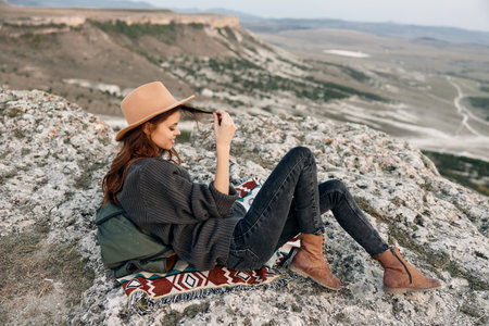 Adventurous woman enjoying the spectacular mountain view with backpack and hat on top of a rockの写真素材